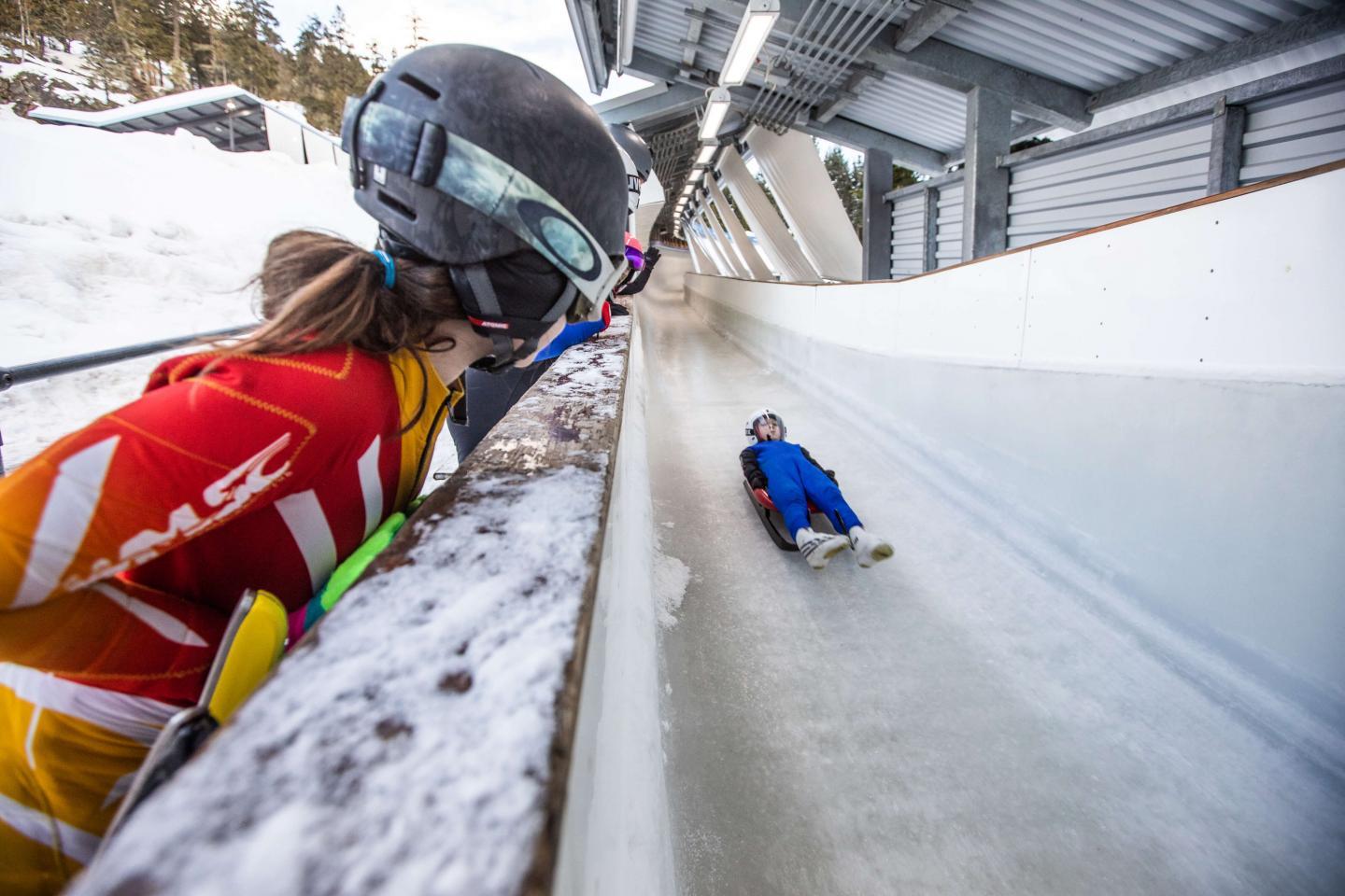kid on luge with fellow athlete watching some sidelines