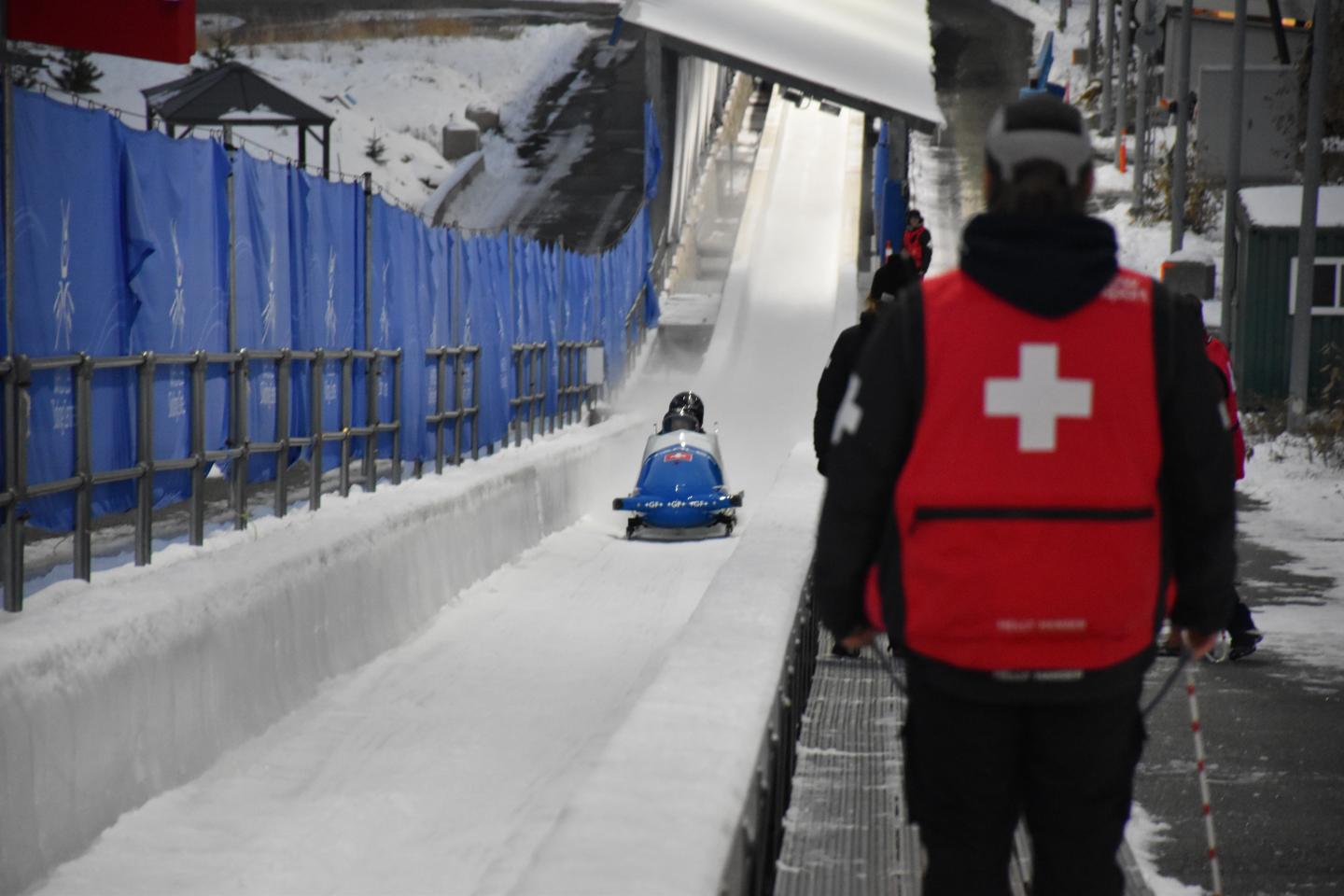 athlete racing down the track with volunteer medic facing them from sidelines