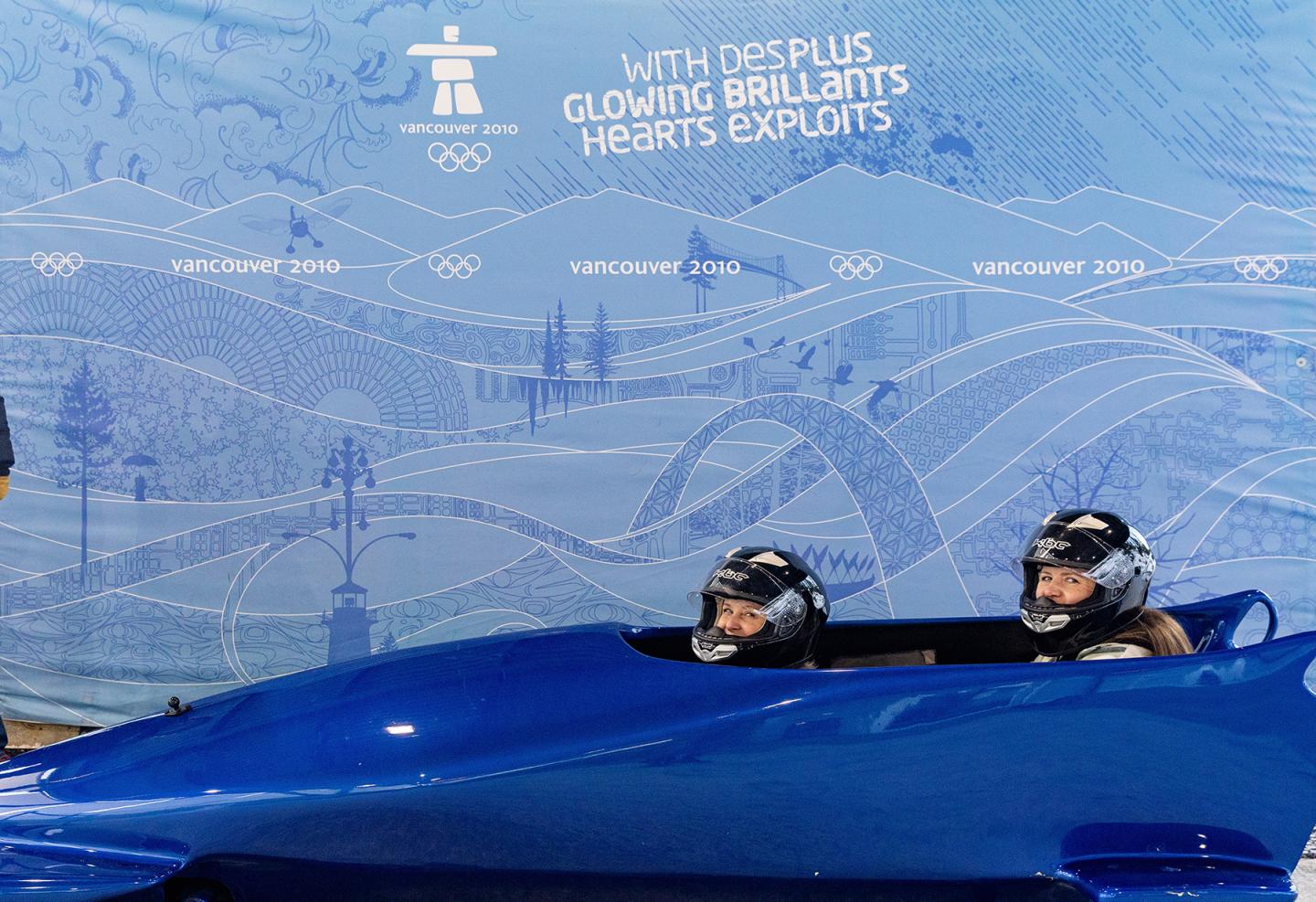 Discover Bobsleigh Public Experience in a blue bobsled against a blue scenic background.