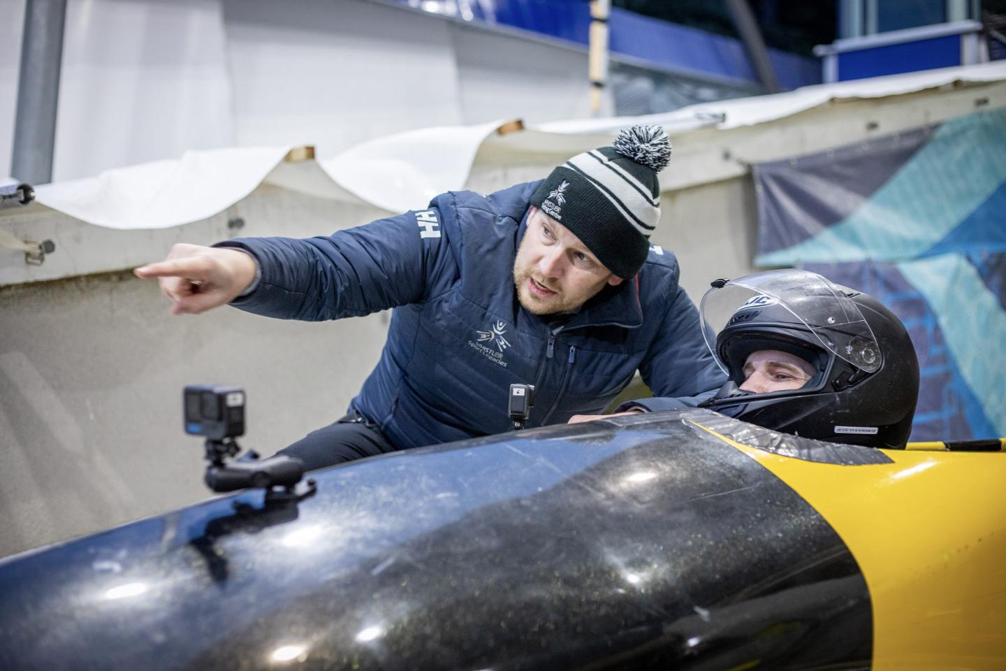 Coach points while talking to athlete in bobsled