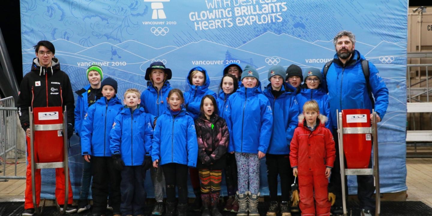 Group of people in blue jackets posing with red sleds on a winter scene backdrop.
