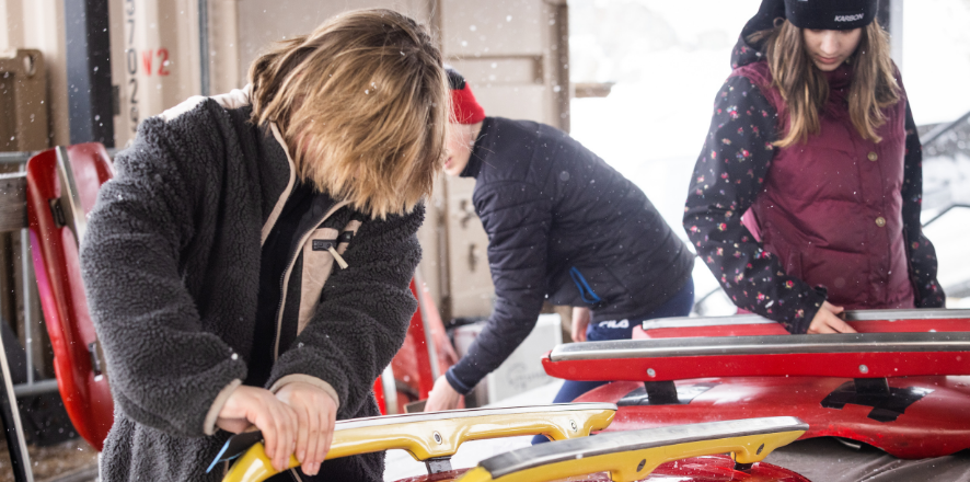 People preparing Luge sleds in a snowy workshop.
