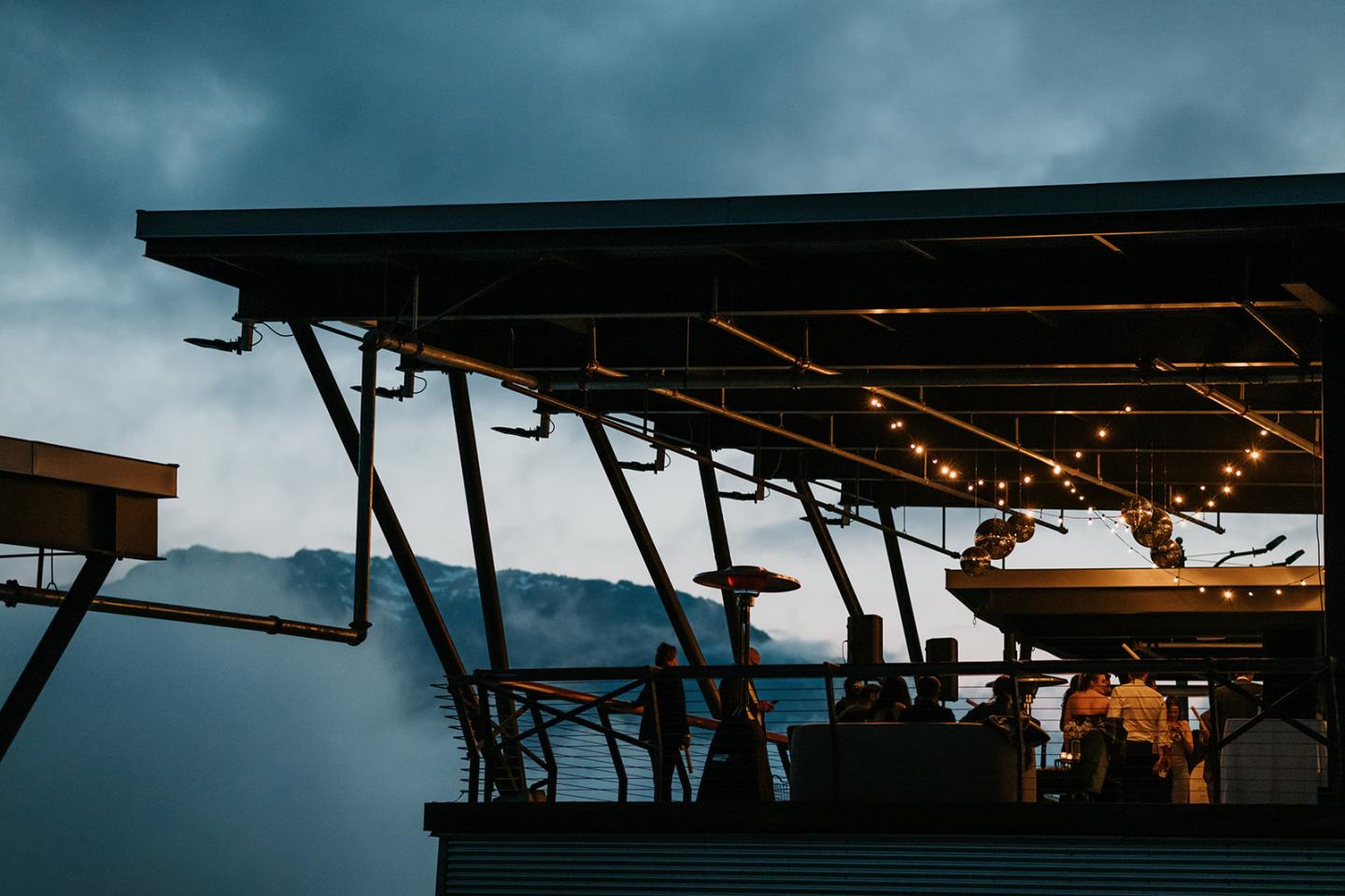 Rooftop restaurant with warm lights at dusk, under a cloudy sky.