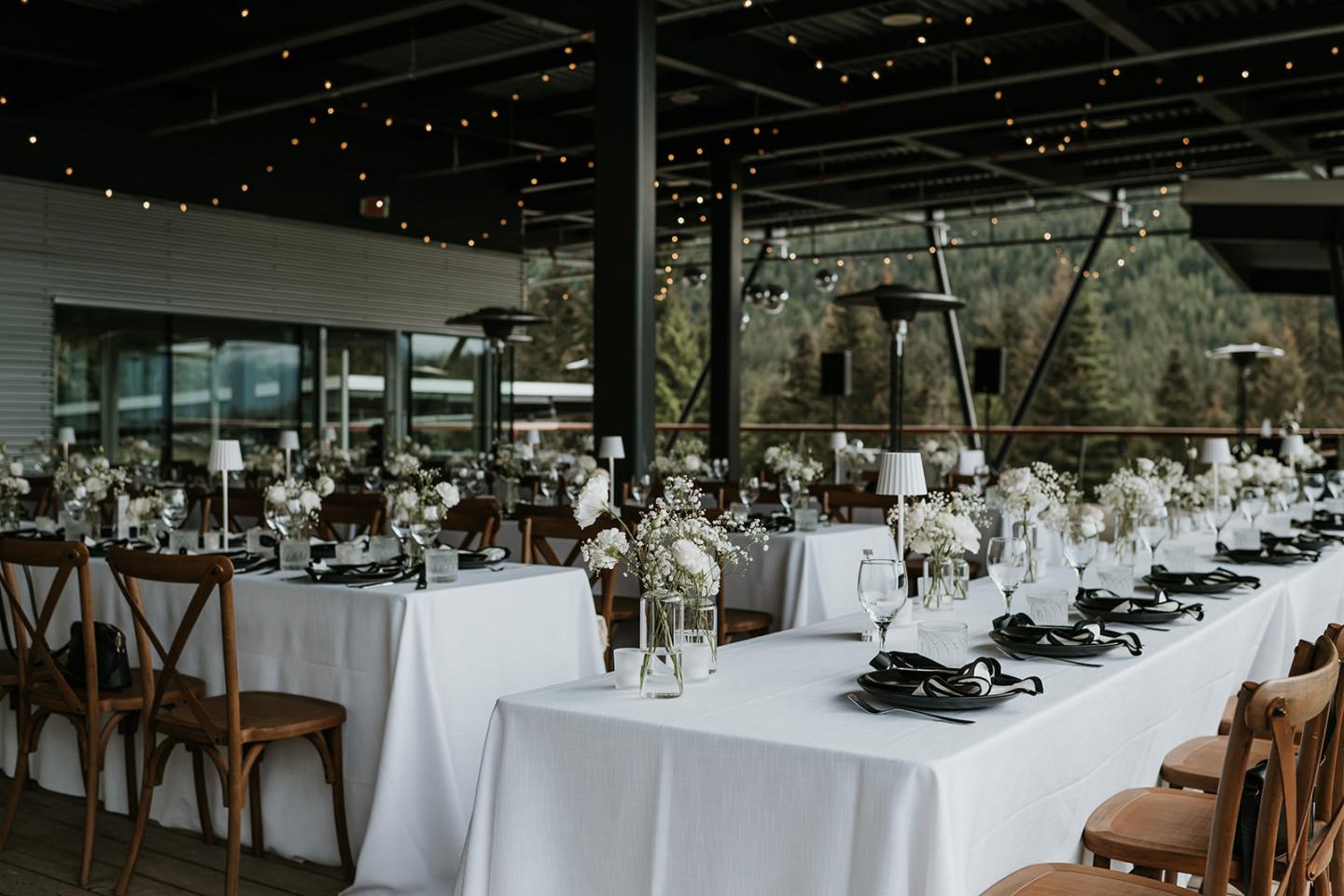 Wedding reception set up with white tablecloths and floral centerpieces under string lights.
