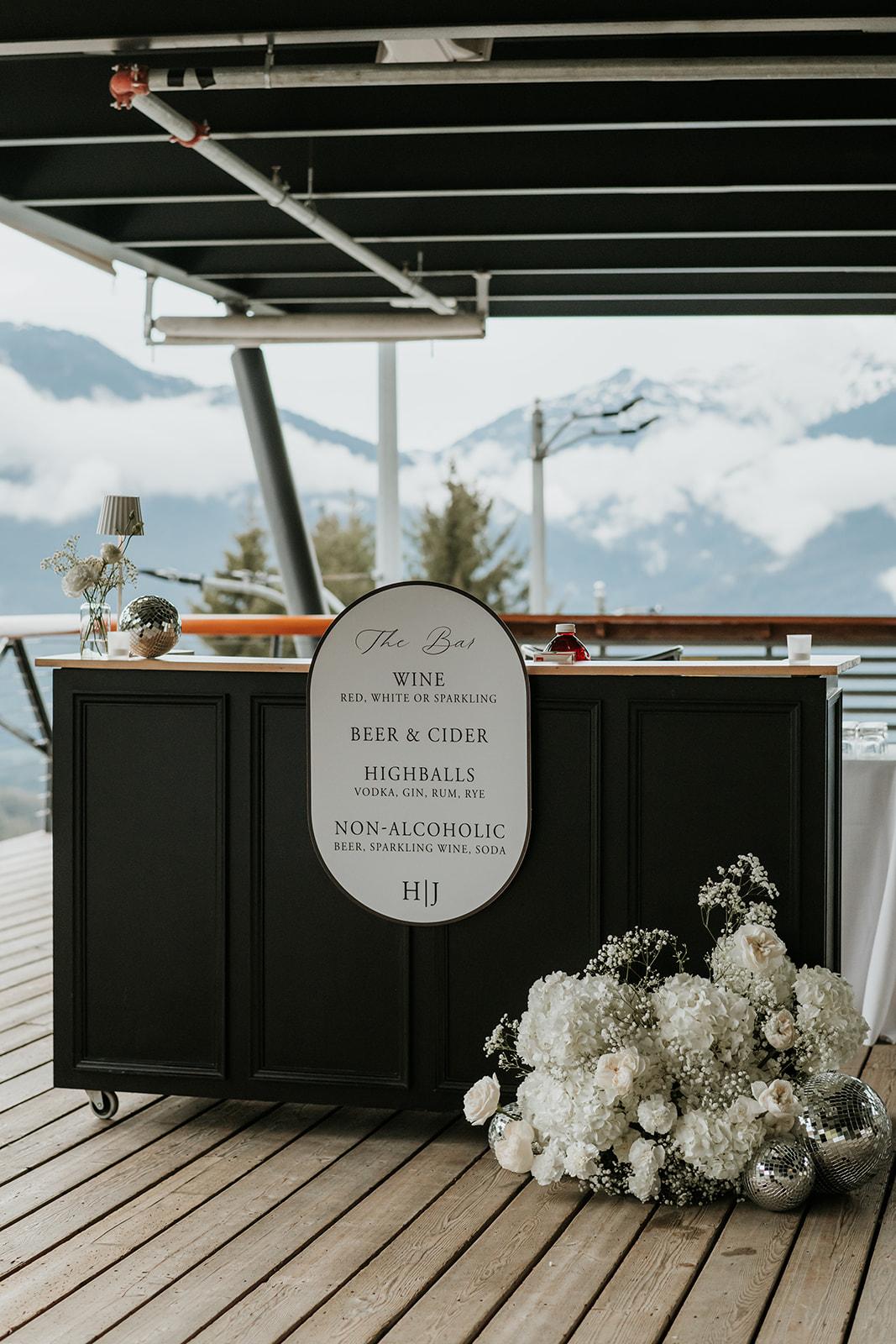 Bar with white flowers, mountain view, dark counter, and sign in front.
