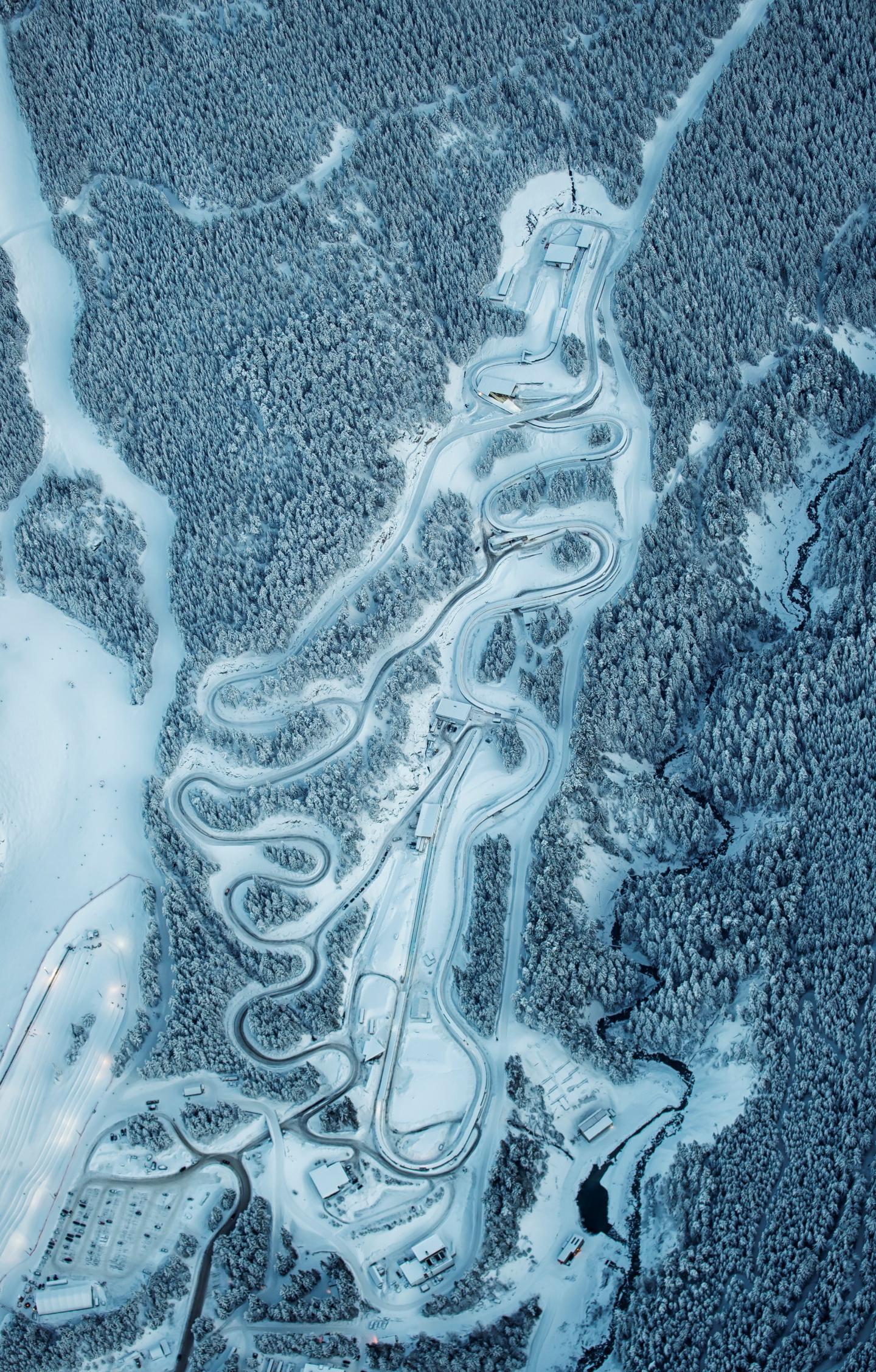 Aerial view of a snowy winding road through dense forest.