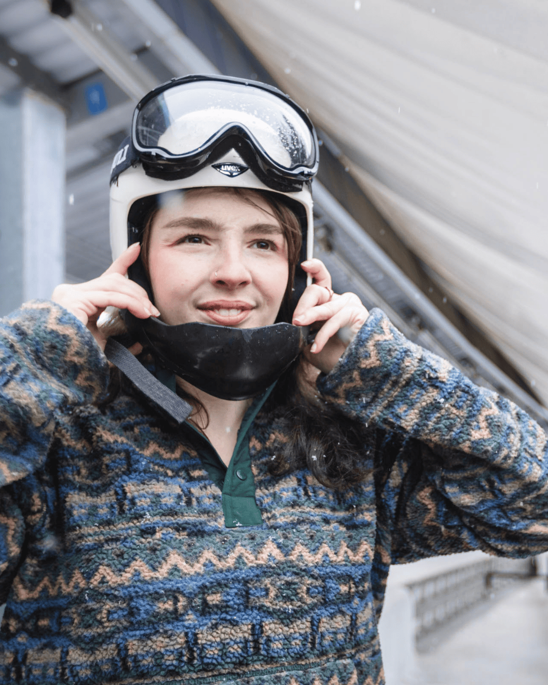 Smiling person wearing a ski helmet and goggles outdoors.