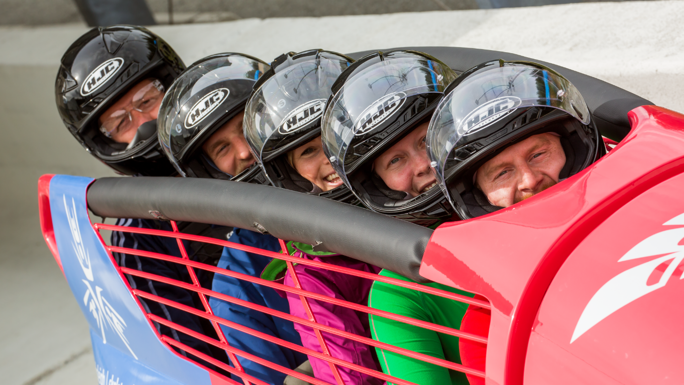 Five smiling people in helmets inside a bobsled.