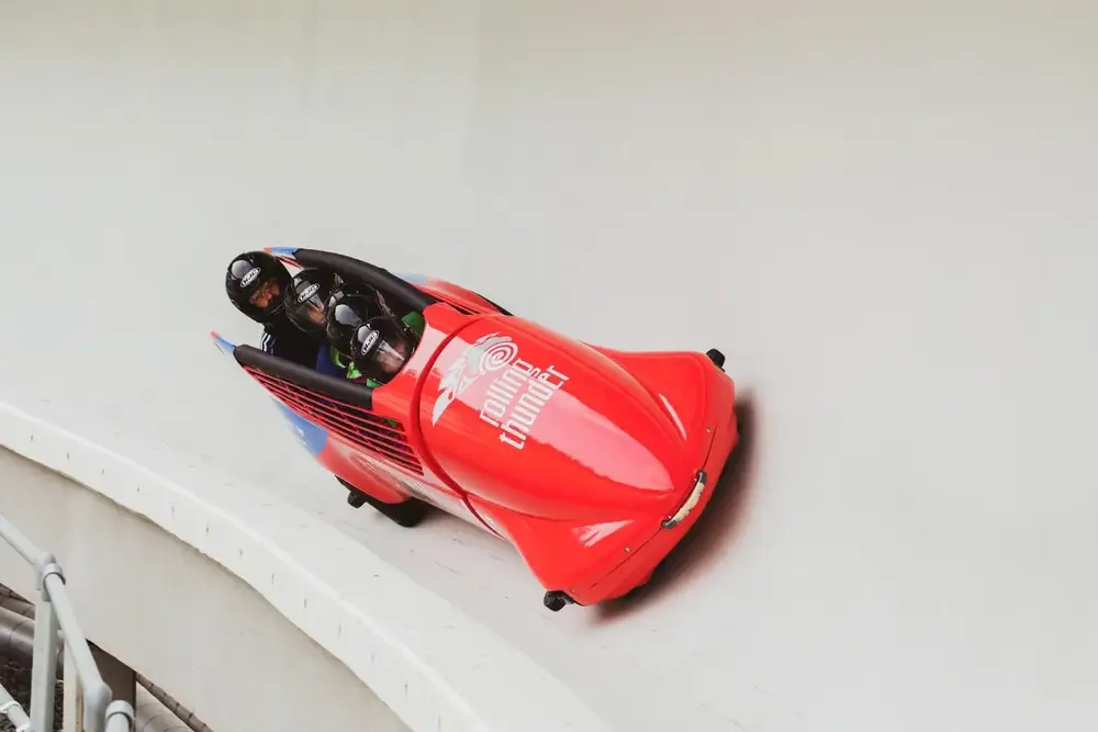 Red bobsled racing down an icy track with two athletes inside.